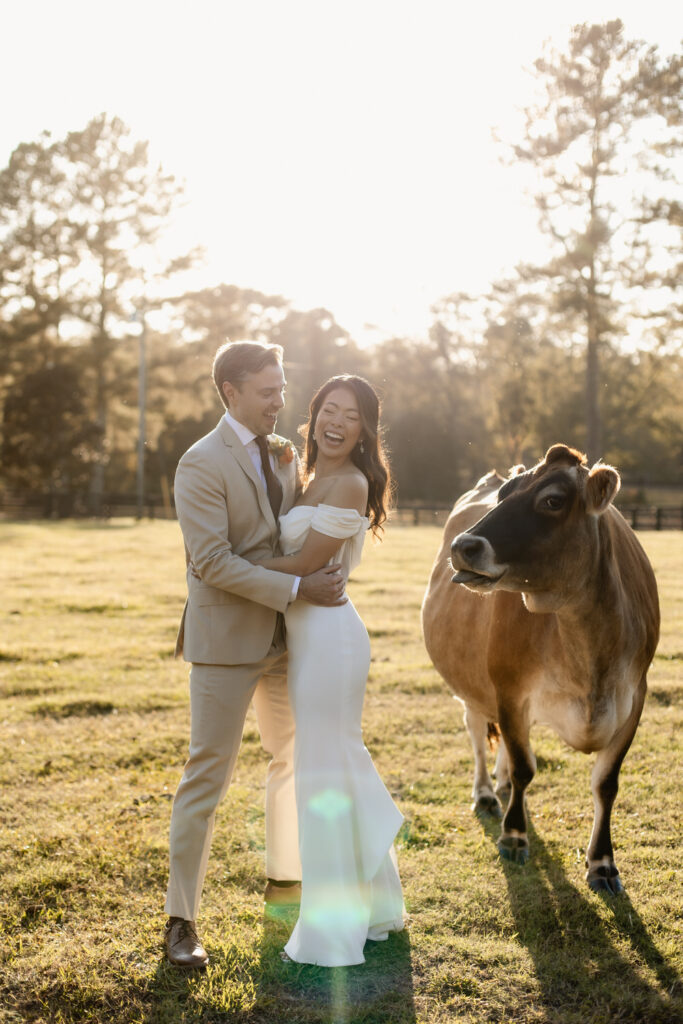bride and groom laughing with cow at Cherry Hollow Farm, a wedding venue in Georgia