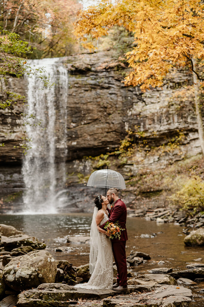 couple kissing beneath a waterfall with fall colors at Cloudland Canyon during their elopemnet